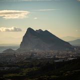 Unter leicht bewölktem Himmel ist ein Felsenmassiv zu sehen, an dessen Fuß eine Stadt liegt