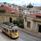 Eine gelbe, alte Straßenbahn biegt in einer Altstadt um eine Ecke