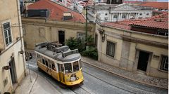 Eine gelbe, alte Straßenbahn biegt in einer Altstadt um eine Ecke