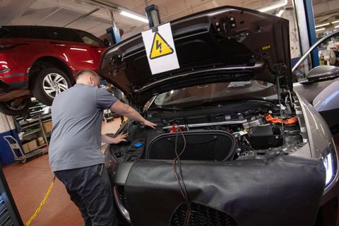 Ein KFZ-Mechaniker wartet in einer KFZ-Werkstatt ein Elektroauto