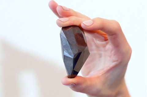 Die rechte Hand einer weißen Frau hält einen schwarzen, ungewöhnlich geschliffenen Diamanten zwischen Daumen und Mittelfinger