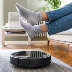 Ein Mensch hebt seine Füße über einen Saugroboter