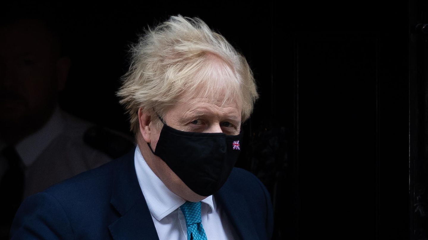 Boris Johnson kommt in Anzug und Krawatte aus einem dunklen Hausflur ins Freie
