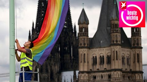 Eine Regenbogenfahne vor dem Kölner Dom und der Kirche Groß St. Martin