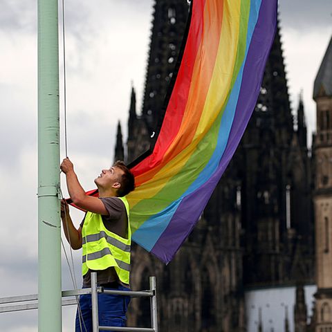 Eine Regenbogenfahne vor dem Kölner Dom und der Kirche Groß St. Martin