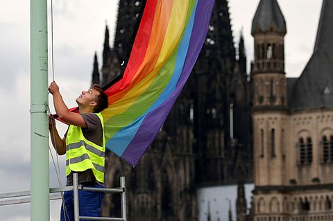 Eine Regenbogenfahne vor dem Kölner Dom und der Kirche Groß St. Martin