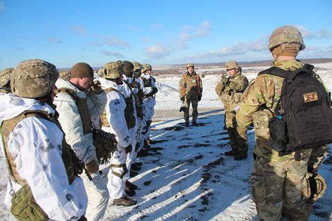 Links steht eine Reihe US-Soldaten in weißen Overalls, vor ihnen drei aus der Ukraine in Tarnfleck