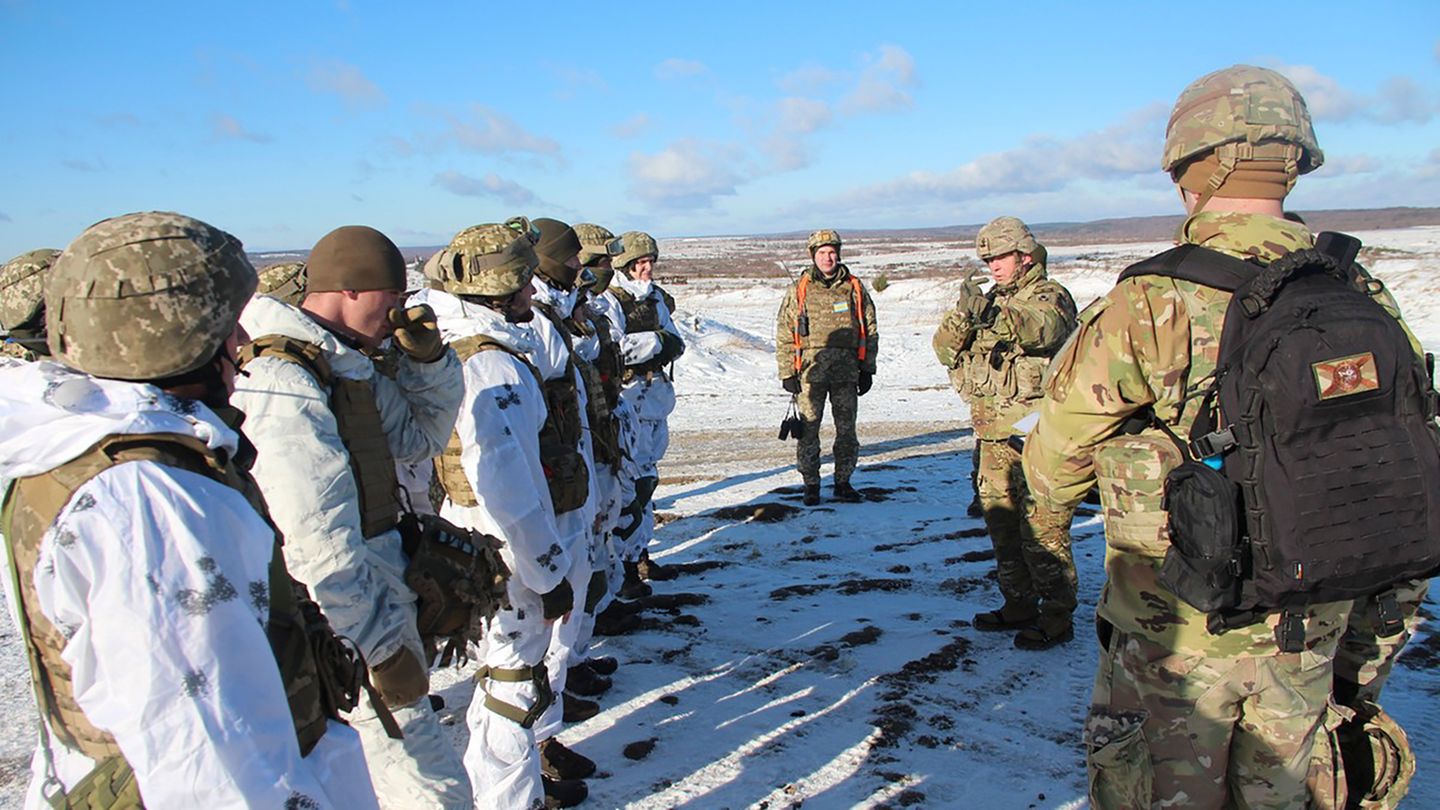 Links steht eine Reihe US-Soldaten in weißen Overalls, vor ihnen drei aus der Ukraine in Tarnfleck