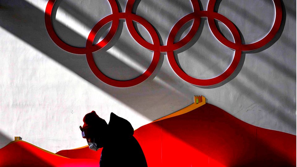 Mann trägt Maske, während er vor Beginn der Wettkämpfe bei der Olympia 2022 in das Skisprungzentrum geht.