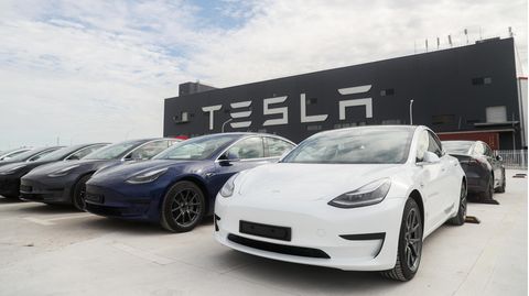 Fahrzeuge von Tesla stehen nebeneinander auf einem Parkplatz vor einem Geschäftsgebäude
