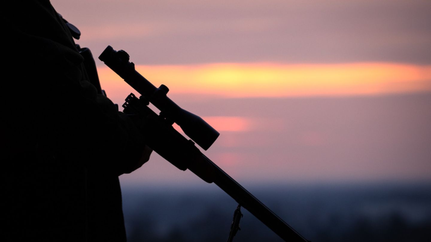 Ein Jäger hält sein Gewehr in der Abenddämmerung