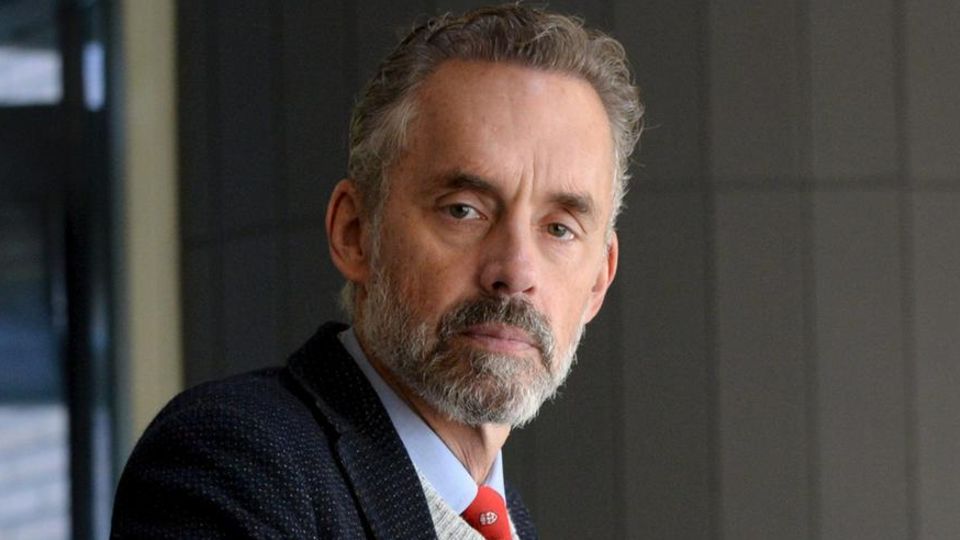 Wearing a tie, shirt and jacket, Jordan B. Peterson looks serious at the camera