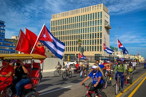 Eine Gruppe junger Menschen mit kommunistischen Flaggen fährt an der US-Botschaft in Havanna vorbei.