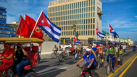 Eine Gruppe junger Menschen mit kommunistischen Flaggen fährt an der US-Botschaft in Havanna vorbei.