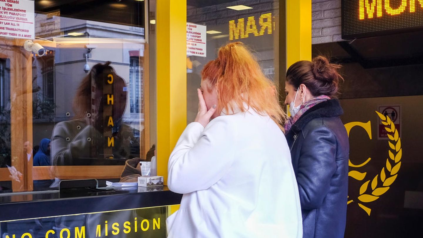 Zwei Frauen betrachten durch die Scheibe einer Wechselstube die Währungskurse, eine fasst sich ins Gesicht