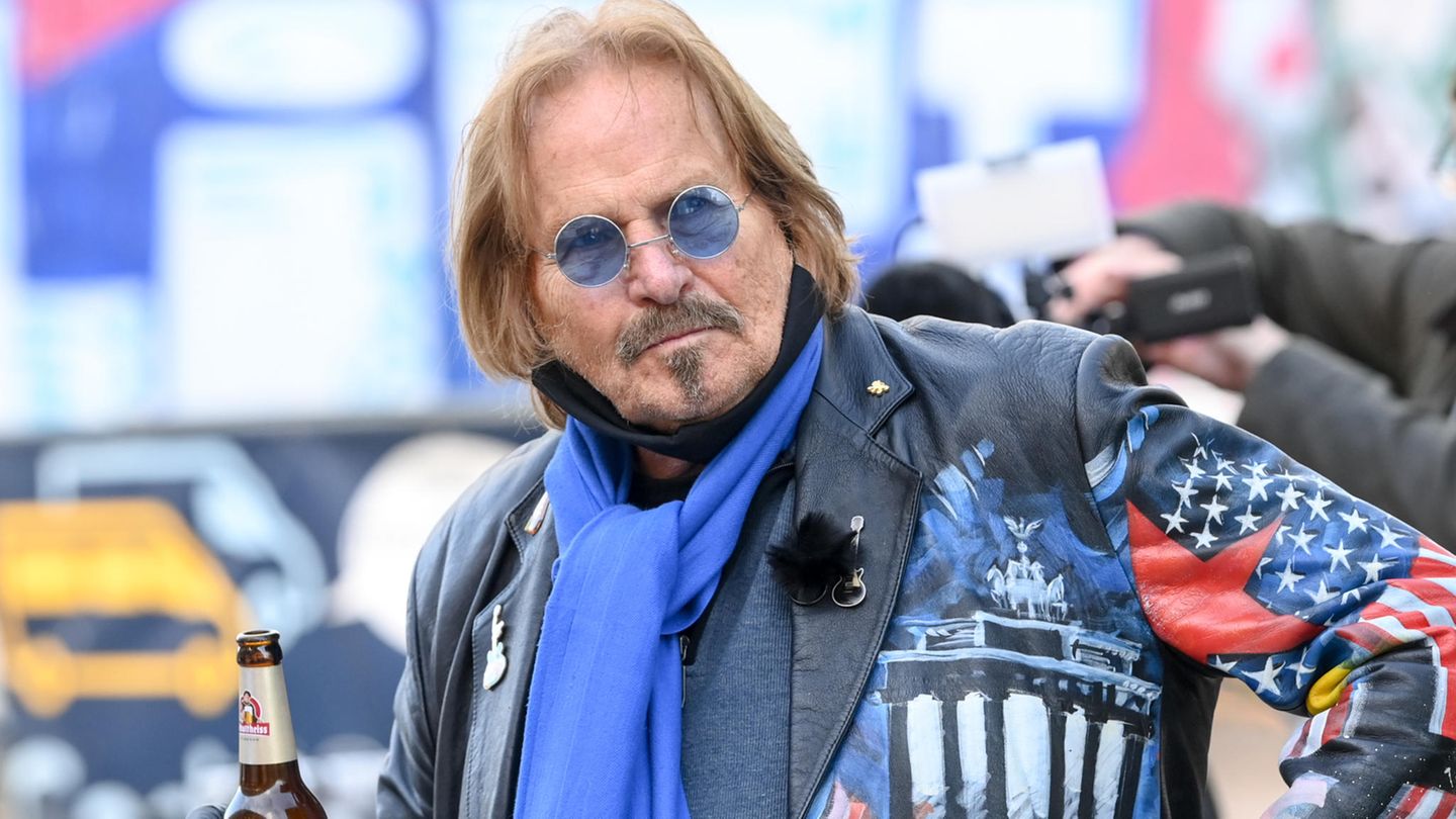 Frank Zander trägt eine bunte Lederjacke und hält eine Flasche Bier in der rechten Hand