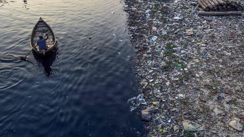 Ein Mann rudert in Dhaka, Bangladesch, an Plastikmüll vorbei