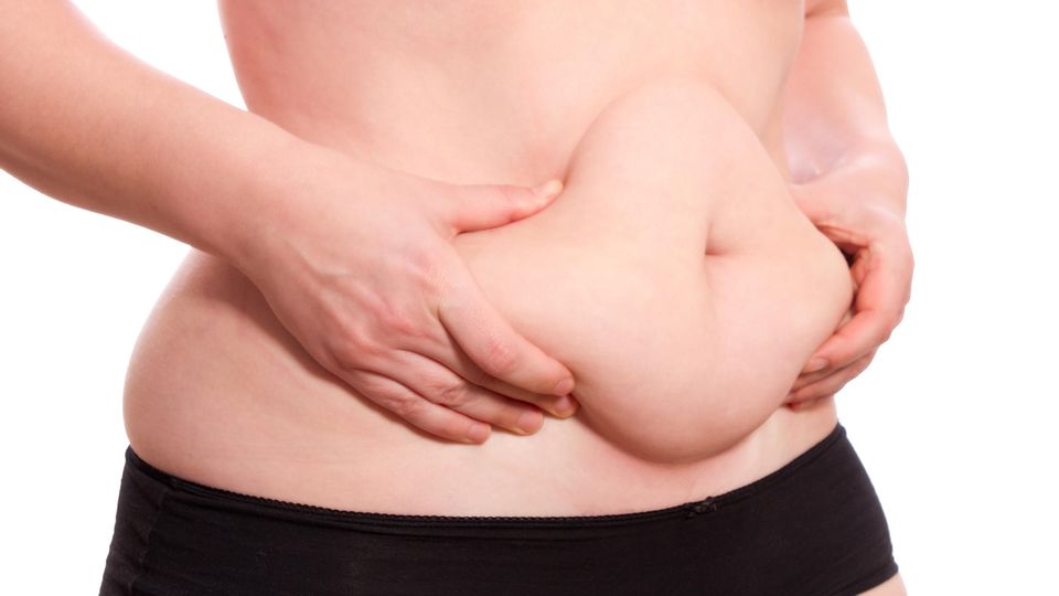 Eine Frau umfasst die Fettpolster an ihrem Bauch