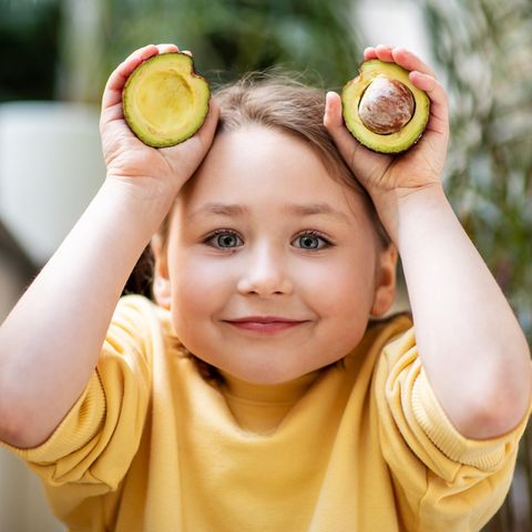 Ein Mädchen hält eine aufgeschnittene Avocado in den Händen