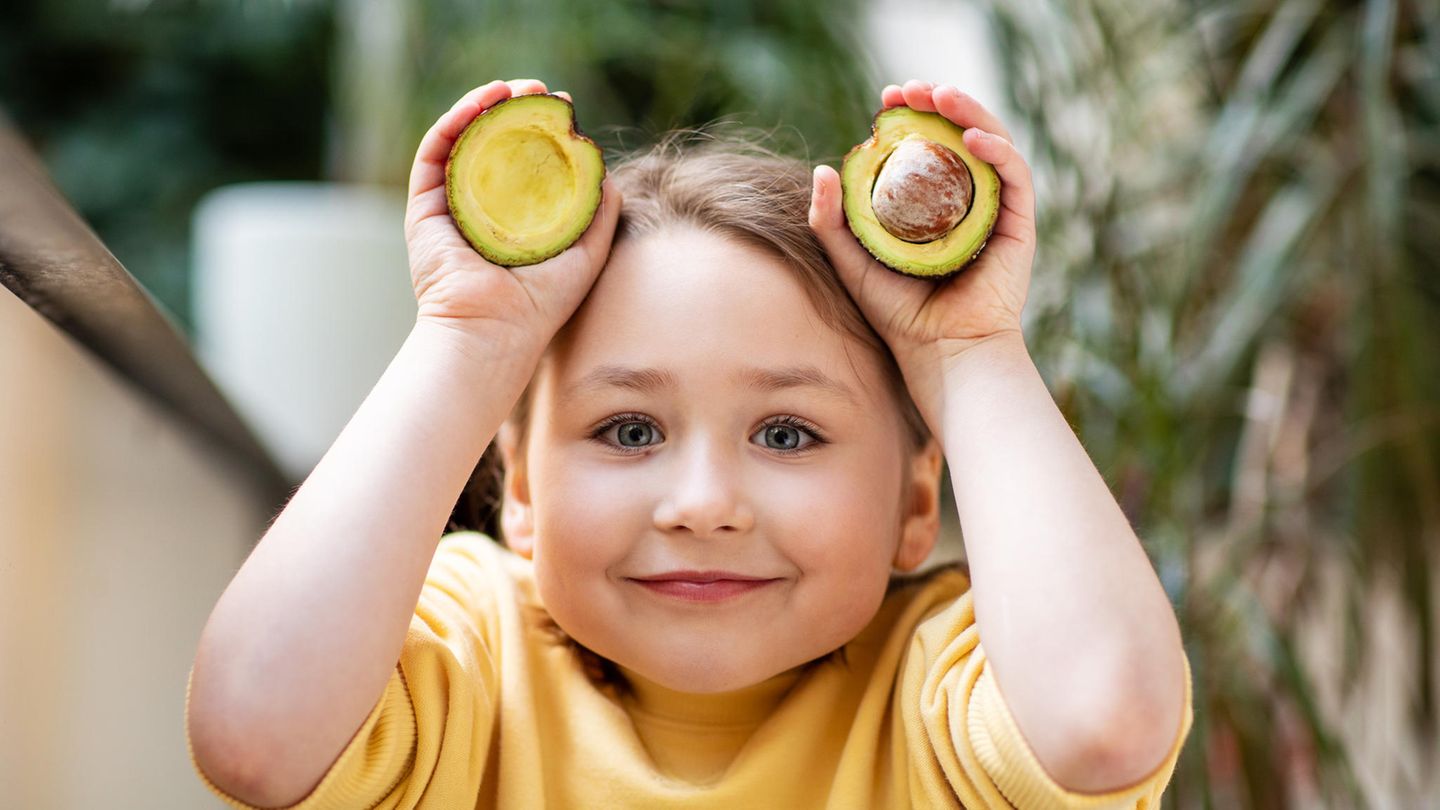 Ein Mädchen hält eine aufgeschnittene Avocado in den Händen
