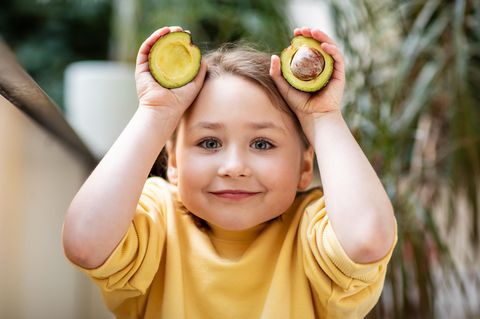 Ein Mädchen hält eine aufgeschnittene Avocado in den Händen