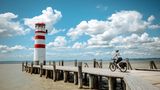 Eine runde Sache: Neusiedler See Radweg  Rust – Podersdorf oder Purbach – "Neusiedl am See  Der Vorteil an Rundwegen: Man kann starten, wo man möchte, und kommt doch überall vorbei. Rust aber, ein kleines Städtchen auf der Westseite des Neusiedler Sees, ist besonders empfehlenswert als Startpunkt am frühen Morgen: Wenn die Störche in ihren Nestern erwachen, paddeln wir aus der Ruster Bucht hinaus auf den größten See Österreichs. Wobei wir uns eher in fernen Gefilden wähnen. Luftsprünge erlaubt, bei Hechtsprüngen Vorsicht: Der See ist nirgends tiefer als 1,80 Meter. Wieder am Ufer, lässt man die Windrichtung entscheiden, wohin der Lenker zeigen soll. Nach Süden? Dann kürzt man in Mörbisch per Fähre nach Illmitz ab und ist plötzlich mittendrin im Nationalpark: zwischen Salzlacken und Schilf und Reihern und Löfflern, die ihren Geschäften nachgehen und Futter suchen. Das sollte man auch.  Mögliche Fundstelle: in Podersdorf, im Gastgarten "Zur Dankbarkeit", könnte es zum Beispiel ein gebratener Zander mit einem Glas Muskateller sein. Ist man dagegen von Rust nach Norden gestartet, sollte man ein Mittagessen in Purbach anpeilen. Beim Spritzwein in einem der 50 kühlen Weinkeller der Purbacher Kellergasse ist die Gefahr allerdings groß, selbst zum Löffler zu werden und den Schnabel zu tief ins Glas zu stecken. Passiert? Das nächste Seebad für einen Mittagsschlaf ist nicht weit. Es reicht, zum Sonnenuntergang in Neusiedl am See zu sein. Der lässt sich übrigens auf die Minute bestimmen: Die Bar "Mole West" bietet die Sonnenuntergangszeit immer aktuell auf ihrer Startseite an. Damit man spätestens um beispielsweise 18.33 Uhr auf der Seeterrasse ein Glas Welschriesling in der Hand hält.