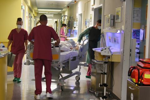 Pfleger schieben einen Corona-Patienten in einem Bett über den Flur einer Klinik