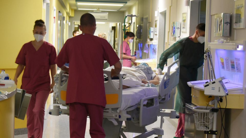 Pfleger schieben einen Corona-Patienten in einem Bett über den Flur einer Klinik