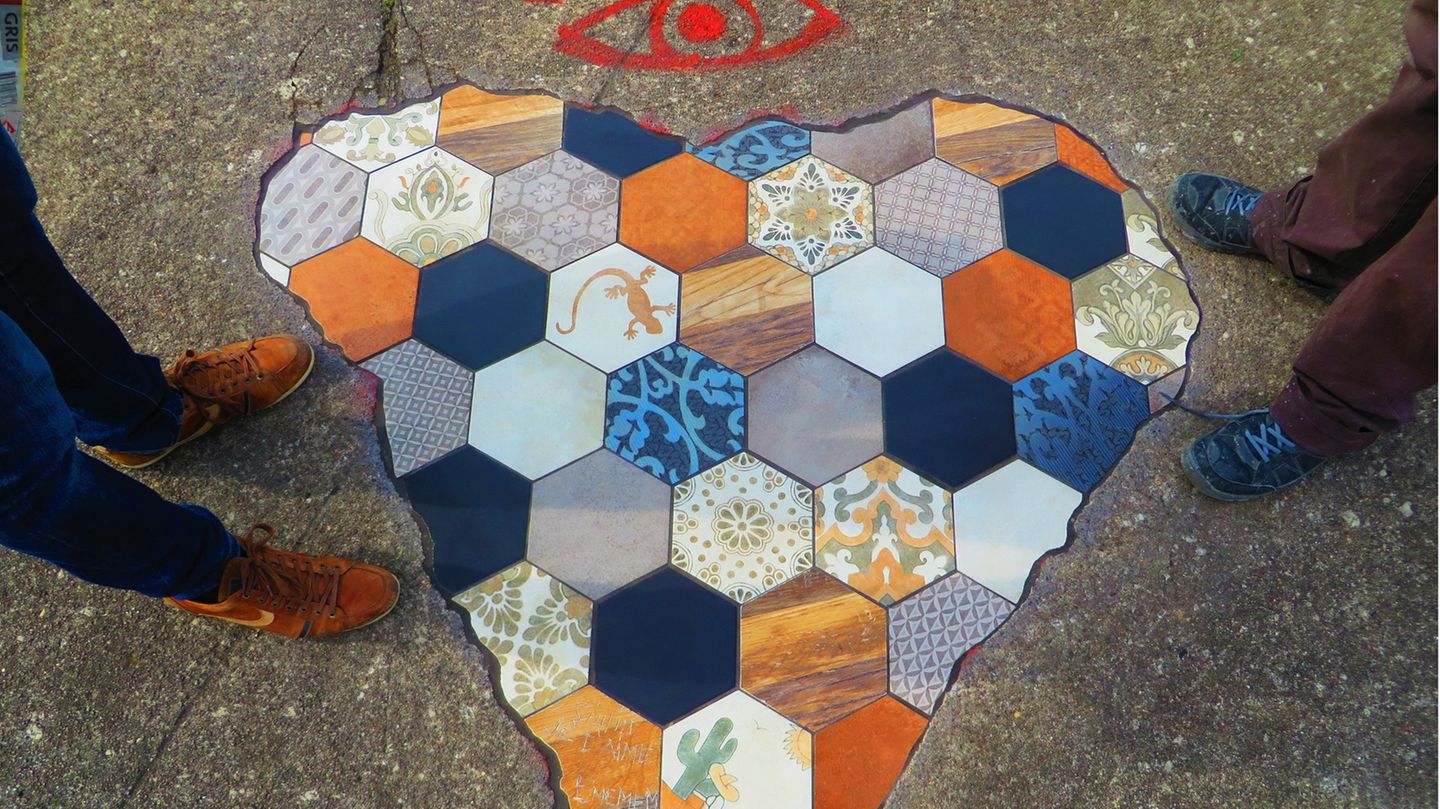 Zwei Menschen stehen neben einem Mosaik in Herzform, das Streetart-Künstler Ememem erstellt hat.