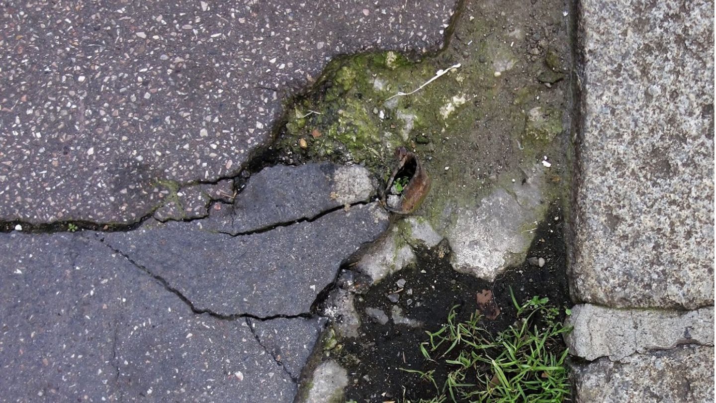 Ein Bürgersteig mit mehreren Rissen, aus denen Gras wächst