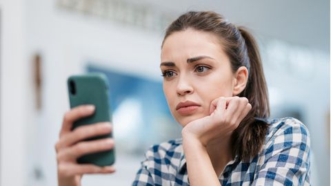 Frau sitzt besorgt vor ihrem iPhone