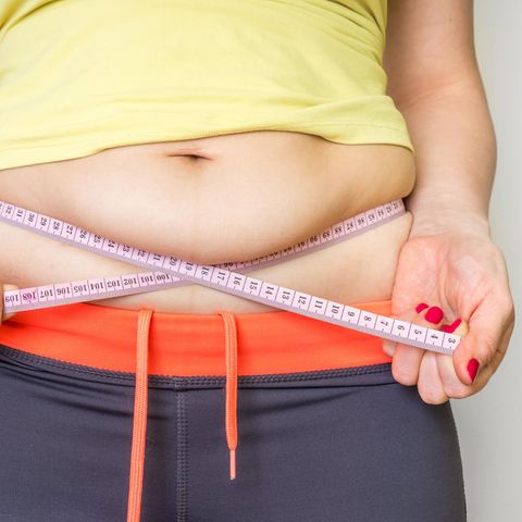 Frau zeigt ihren Bauch mit einem Maßband