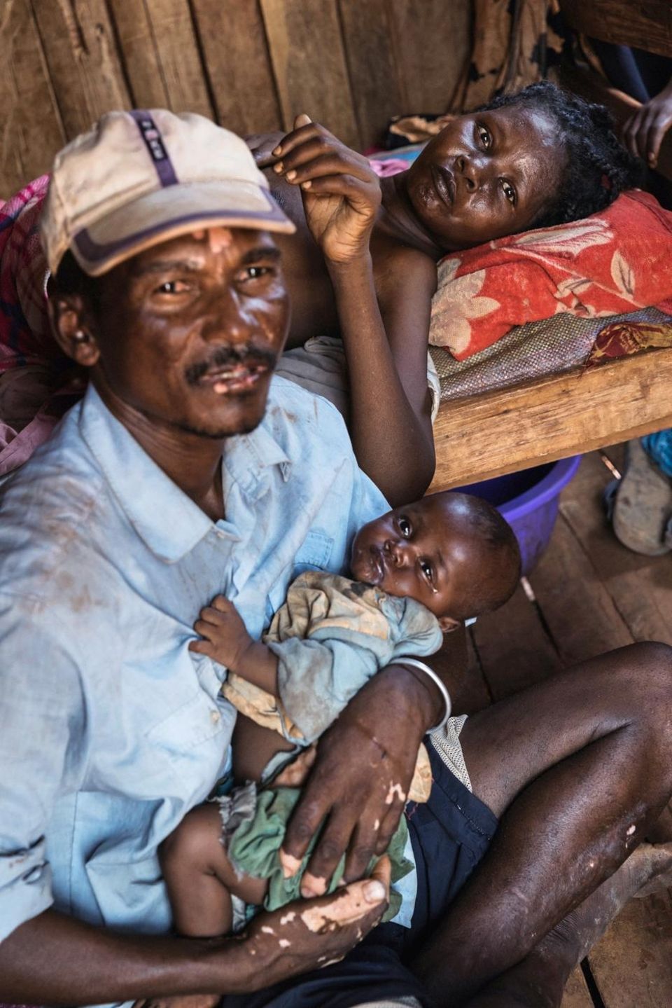 Kein Regen, keine Ernte: Ein Vater hält sein Baby im Arm. Auf dem Bett dahinter liegt die unterernährte Mutter. Sie ist zu schwach zum Stillen Ein Vater hält sein Baby im Arm. Auf dem Bett dahinter liegt die unterernährte Mutter. Sie ist zu schwach zum Stillen