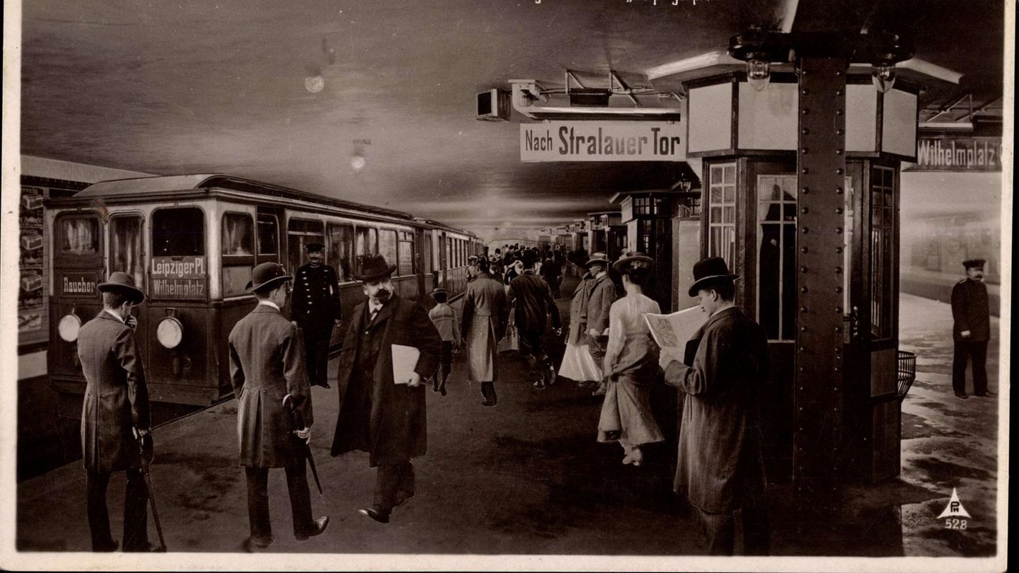 Ein Mann mit Hut liest Zeitung am Untergrundbahnhof Leipzigerplatz. Andere Menschen steigen in die U-Bahn ein. Foto von 1935.