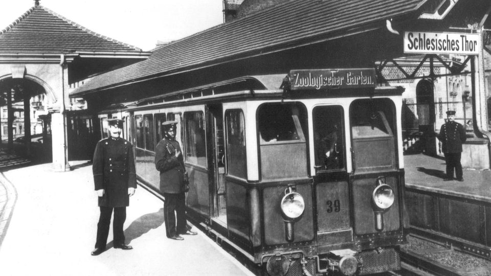 Zwei Schaffner mit Hut  stehen im Jahr 1902 vor der ersten U-Bahn, die damals in Berlin in Betrieb ging.