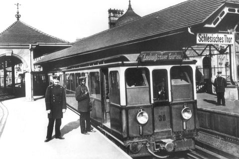 Zwei Schaffner mit Hut  stehen im Jahr 1902 vor der ersten U-Bahn, die damals in Berlin in Betrieb ging.