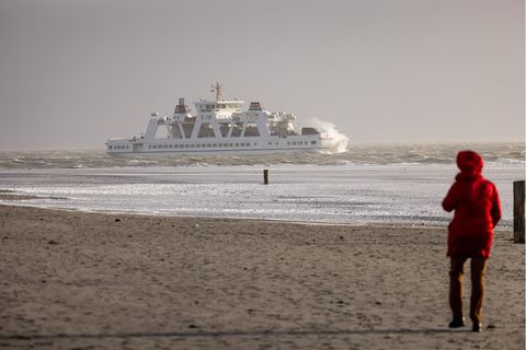 Frau steht am Strand und schaut auf ein Schiff