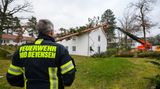 Einsatzkräfte der Freiwilligen Feuerwehr beseitigen über eine Drehleiter einen Baum, der auf einem Gebäude liegt.
