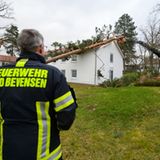 Einsatzkräfte der Freiwilligen Feuerwehr beseitigen über eine Drehleiter einen Baum, der auf einem Gebäude liegt.