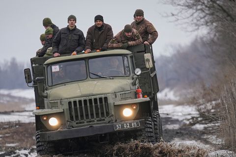 Ukrainische Soldaten stehen auf der Ladefläche eines LKWs, der auf einer schlammigen Straße fährt.