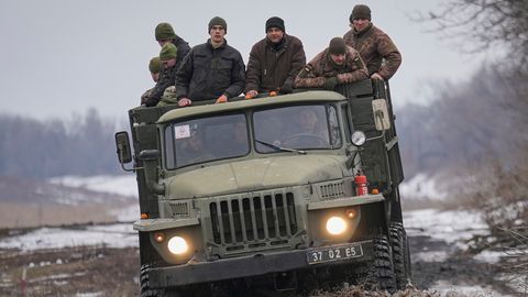 Ukrainische Soldaten stehen auf der Ladefläche eines LKWs, der auf einer schlammigen Straße fährt.