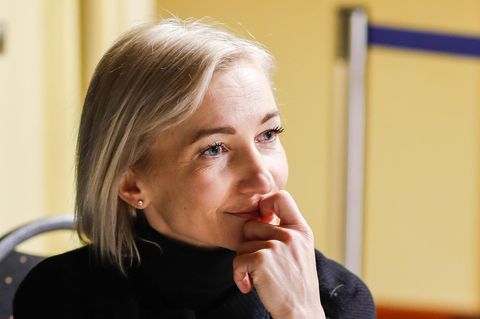 Eine weiße Frau mit schulterlangen blonden Haaren hält sich die linke Hand an den Mund und schaut nachdenklich