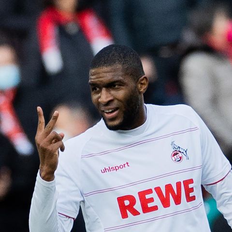 Ein schwarzer Fußballer im weißen Trikot reckt lächelnd Zeige- und Mittelfinger der rechten Hand in die Höhe