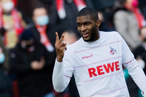 Ein schwarzer Fußballer im weißen Trikot reckt lächelnd Zeige- und Mittelfinger der rechten Hand in die Höhe
