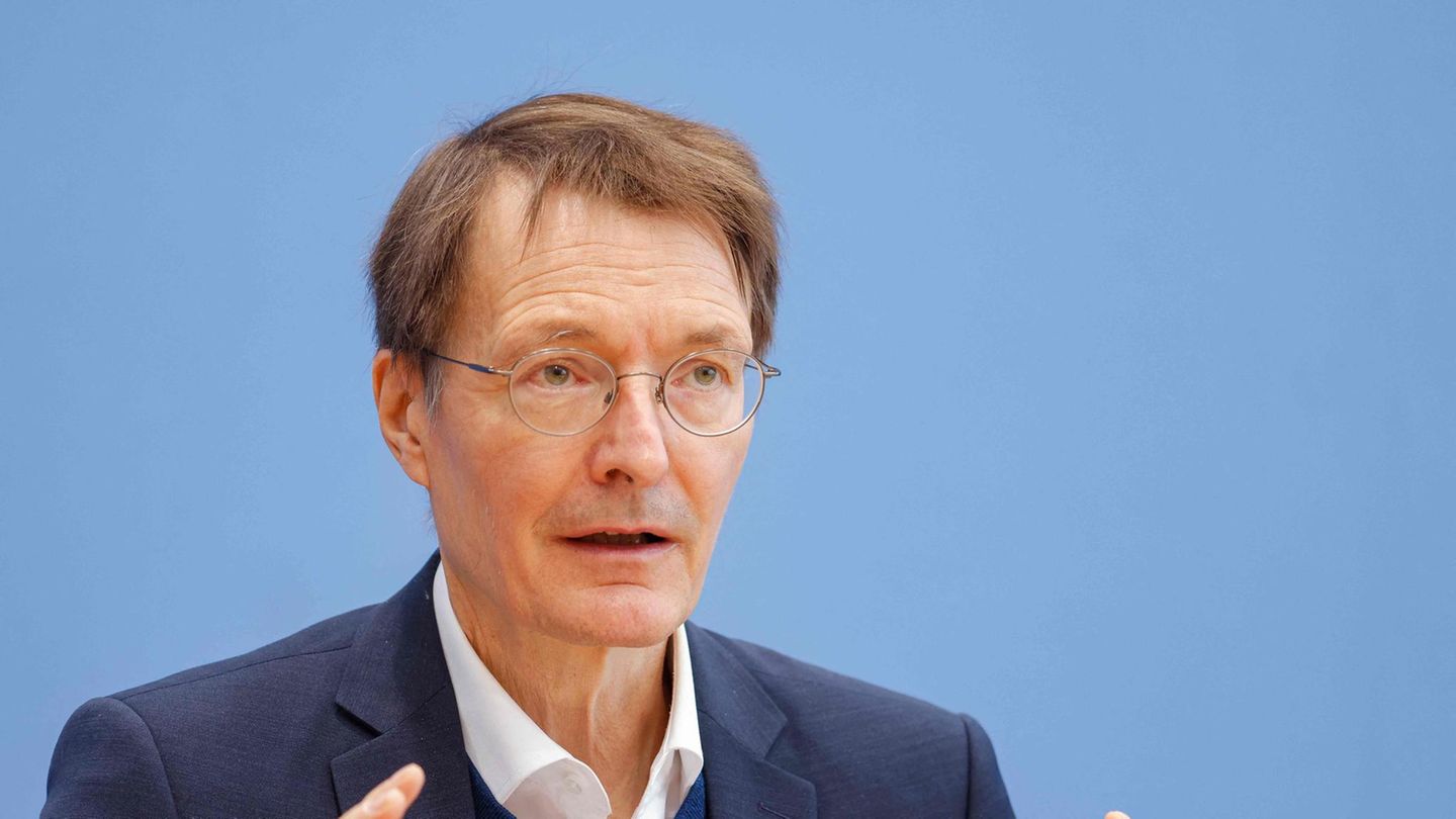 Ein weißer Mann mit braunem Seitenscheitel und runder Metallbrille gestikuliert vor einer blauen Wand