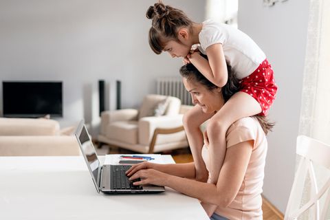 Mutter mit Kind auf den Schultern sitzt vor dem Computer