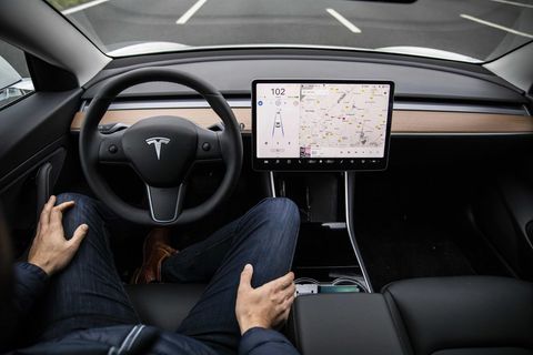 Ein Fahrer sitzt am Steuer eines Tesla-Autos und hat beide Hände auf seinen Beinen abgelegt