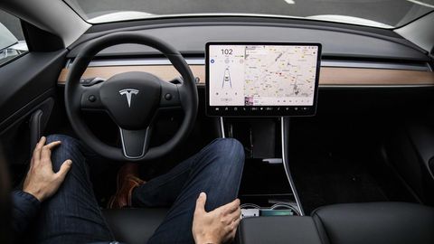 Ein Fahrer sitzt am Steuer eines Tesla-Autos und hat beide Hände auf seinen Beinen abgelegt