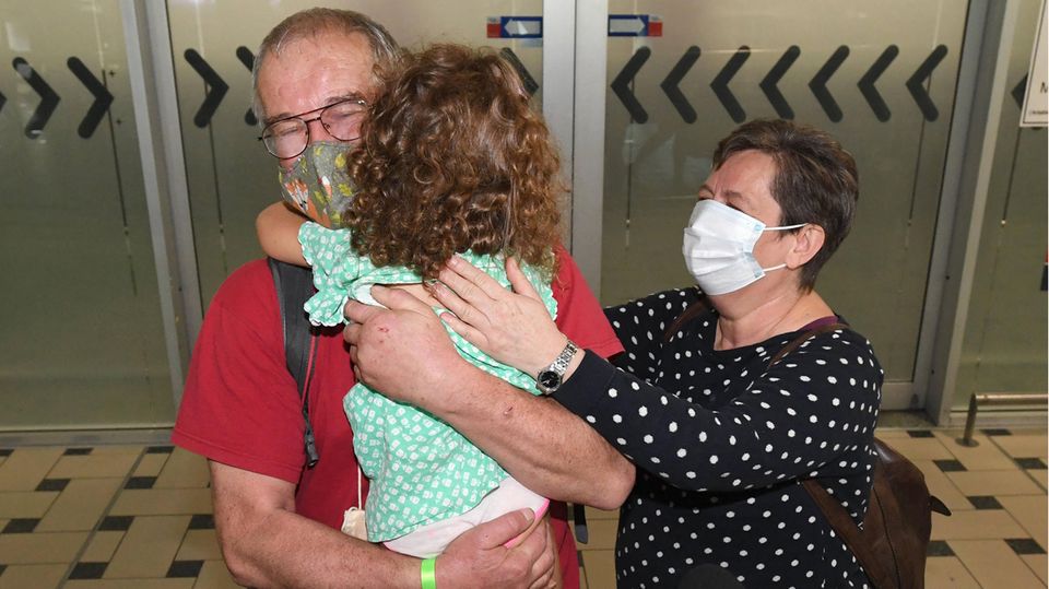 Ein Mann und eine Frau mit Mundschutz umarmen ihre kleine Enkelin Ein Mann und eine Frau mit Mundschutz umarmen ihre kleine Enkelin