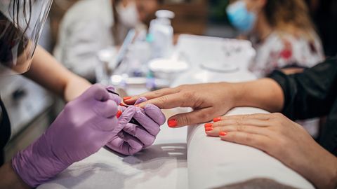 Eine Frau lackiert die Fingernägel einer anderen Frau im Nagelstudio